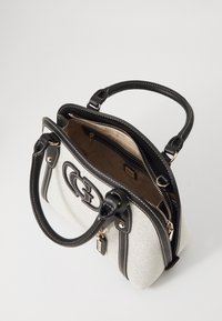 Gros plan sur un sac à main en tissu blanc avec des accents en cuir noir, présentant un logo, des poignées doubles et une ouverture zippée sur le dessus avec des poches intérieures.