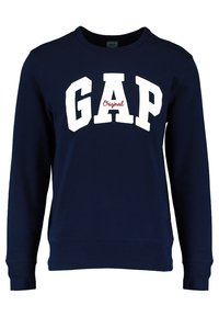 Felpa blu navy con collo a giro, caratterizzata da grande scritta bianca "GAP" e dettagli rossi "Original" sul petto. Materiale in cotone morbido.