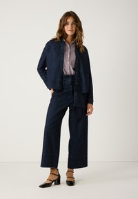 Dunkelblaue Jeansjacke mit Knopfverschluss, zwei Brusttaschen, kombiniert mit passenden weit geschnittenen dunkelblauen Jeans und schwarzen High Heels.