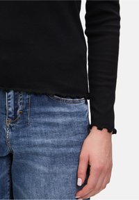 Zwarte geribbelde langekruis top met scalloped zoomdetails, gecombineerd met lichtblauwe spijkerbroek met een voorzak.