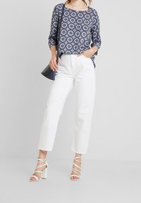 Blusa a fantasia navale con maniche a 3/4, abbinata a jeans bianchi a gamba dritta. Sandali con tacco e fasce bianchi e una borsa nera completano l'outfit.