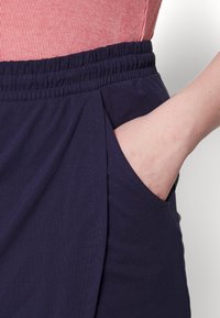 Námořnické modré kalhoty s elastickým pasem, vybavené boční kapsou a hladkou texturou tkaniny. Navrženo s minimem detailů.