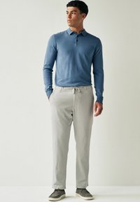 Polo à manches longues bleu clair associé à un pantalon gris clair. Le pantalon possède une taille élastique et une coupe décontractée. Chaussures gris foncé.