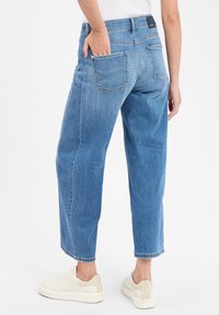 Jean en denim bleu clair avec une coupe décontractée, longueur cropped, deux poches arrière et un ourlet propre. Porté avec des baskets blanches.