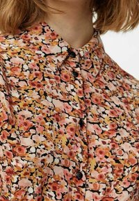 Camicia button-up floreale in tessuto leggero, con un motivo di fiori rosa e arancioni su sfondo nero, colletto alla francese e bottoni neri.