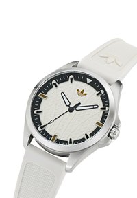 Baltas gumos dirželis su struktūrine baltos spalvos ciferblatu, juodais valandų žymekliais, sidabriniu korpusu ir auksiniu logotipu. Yra juodų bezelio akcentų.