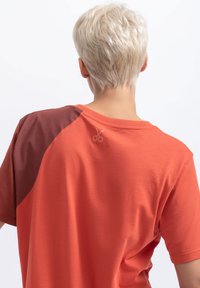 Korte mouwen t-shirt in oranje met een bruine schouderpaneel. Bevat een subtiele schaar-logo op de achterkant, gemaakt van zachte katoen stof.