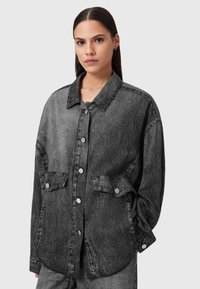 Giacca di jeans nera con vestibilità rilassata, colletto a punta, bottoni a pressione argento, tasche sul petto e finitura in tessuto testurizzato.