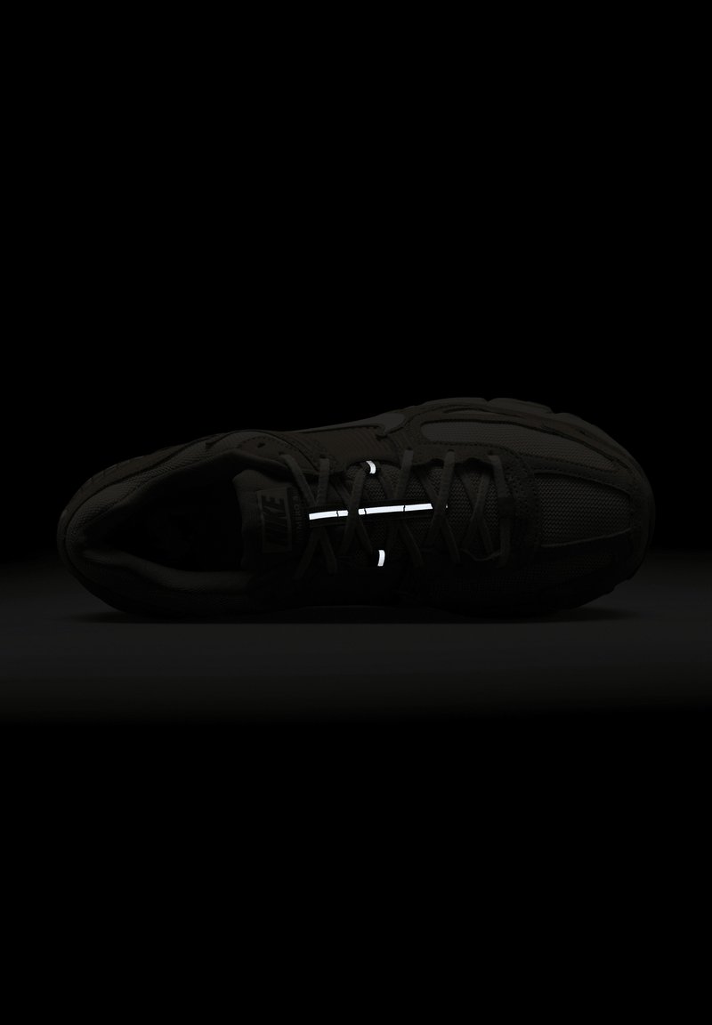 Zapatilla negra con upper de tejido texturizado, cordones reflectantes y diseño de punta redondeada. Estilo minimalista con una apariencia sin costuras.