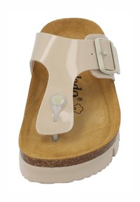 Beige patenteret lædersandal med tåpost og spænde, der har en korkfodbed og tekstureret tan indersål. Flad såldesign.