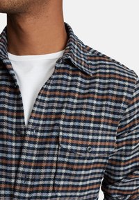 Rutigt flanellskjorta med marinblå, grå och orange ränder. Knappad ficka och krage i en mjuk, texturerad tyg.