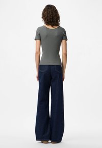 Top cinza de manga curta com textura em nervuras, combinado com calças de ganga escuras de cintura alta e perna larga, apresentando bolsos traseiros e um corte relaxado.