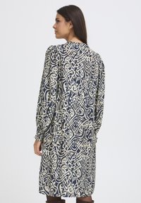 Langärmeliges Kleid in Marineblau mit abstraktem Creme-Muster, das einen figurbetonten Oberteil, eine lockere Silhouette und geraffte Bündchen aufweist. Glatte Stofftextur.