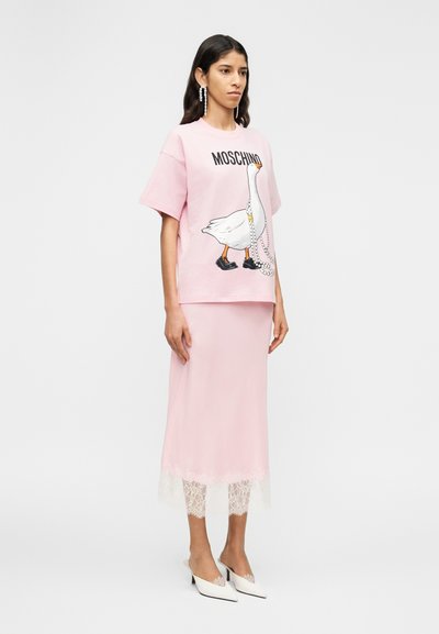 Ροζ μπλουζάκι με κινούμενη εικόνα πάπιας και το κείμενο "Moschino", συνδυασμένο με ροζ φούστα slip με δαντελένιο τελείωμα και λευκά μυτερά παπούτσια.