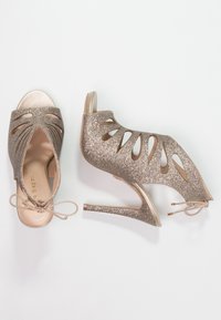 Kasut tinggi berkilau berwarna tembaga dengan pola potongan dan permukaan seperti satin. Dilengkapi dengan tali dan tumit stiletto yang runcing.