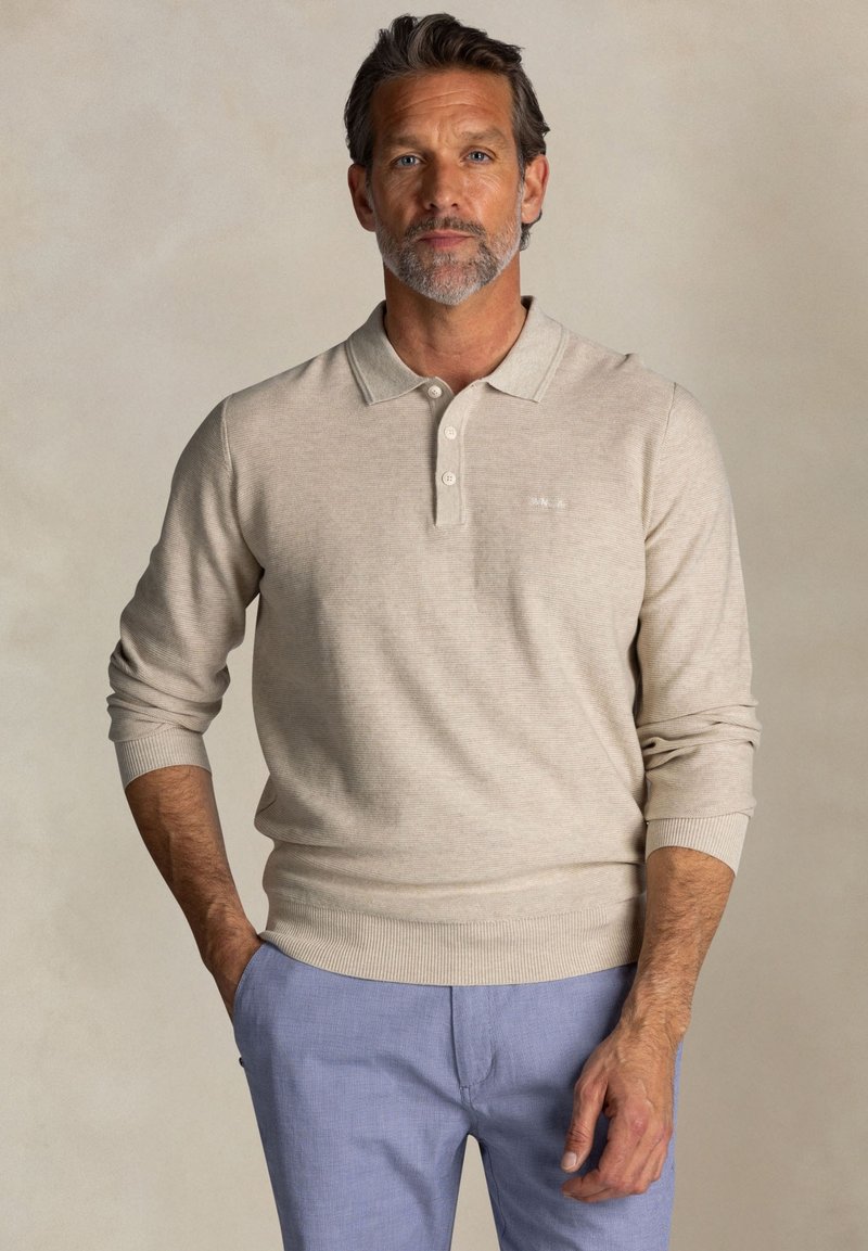 Beige poloshirt met lange mouwen, een kraag en drie knopen, voorzien van een ribbelzoom en manchetten. Tekkere stof met subtiele stiksels.