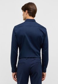Een marineblauwe lange mouwen shirt met een gladde textuur, voorzien van een klassiek kraag en knoopmanchetten, gecombineerd met bijpassende broek.