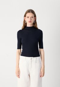 Mørkeblå ribbet turtleneck topp med korte ermer, med en tettsittende design og teksturert stoff. Båret med lysfargede høytlivsbukser.