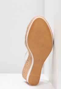 Semelle de sandale compensée avec talon en liège, semelle extérieure en caoutchouc tan, semelle intermédiaire blanche et marquage taille 37, posée sur des surfaces blanches.