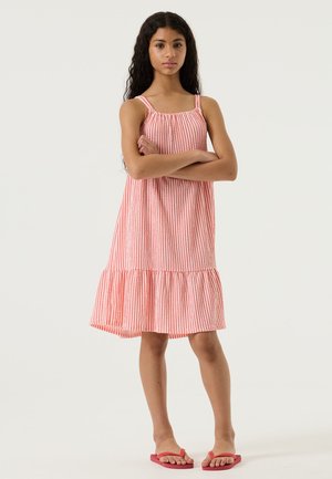 Vestito a righe rosse e bianche realizzato in tessuto leggero, con orlo svasato e spalline sottili. Abbinato a infradito rosa.