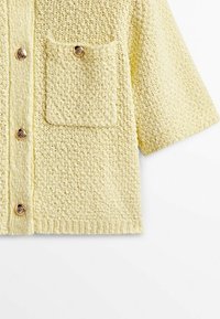 Krótki kardigan z krótkim rękawem z miękkiego, teksturowanego żółtego materiału, z pojedynczą nakładaną kieszonką i pięcioma dekoracyjnymi guzikami.