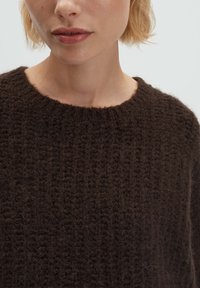 Brauner gestrickter Pullover mit rippenartiger Struktur und weitem Rundhalsausschnitt. Der Stoff wirkt weich und leicht flauschig.