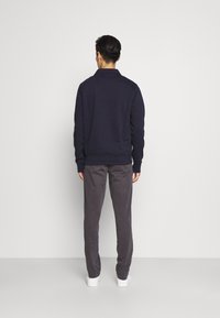 Maglietta a maniche lunghe blu navy con colletto a costine, abbinata a pantaloni grigi. La maglia presenta una vestibilità dritta e un tessuto testurizzato. Sneakers bianche completano l'outfit.