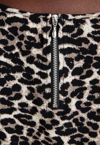 Tecido com padrão de leopardo apresentando um zíper prateado visível nas costas. A textura parece suave e ligeiramente texturizada, com cores preta e bege.