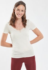 Top crema a maniche corte con scollatura ampia e dettagli in pizzo intricati sulla parte frontale. Materiale morbido e leggero con una forma aderente.