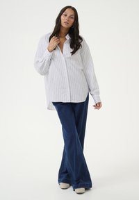 White and light blue striped button-up shirt with long sleeves, paired with flared dark blue jeans and beige shoes, featuring a relaxed fit.