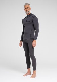 Grå termisk bluse med kvart lynlås og lange ærmer, parret med matchende tætsiddende termiske leggings. Glat tekstur, minimal branding synlig.