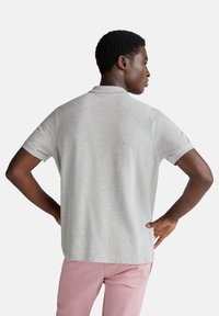 Světlé šedé polo tričko s krátkým rukávem a límečkem; měkká textura a volný střih. V kombinaci se světle růžovými kalhotami.