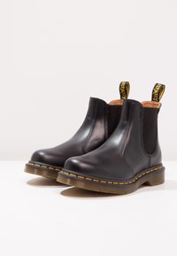 Black leather Chelsea boots with elastic side panels, contrasting yellow stitching, and pull tabs on the heels. Smooth finish and round toe.