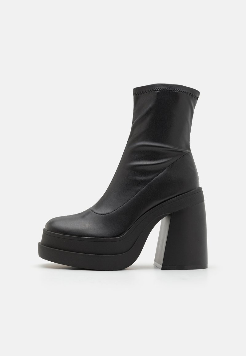 Stivaletto nero in materiale sintetico liscio, con alto tacco a blocco, punta rotonda e parte superiore elastica con texture arricciata.