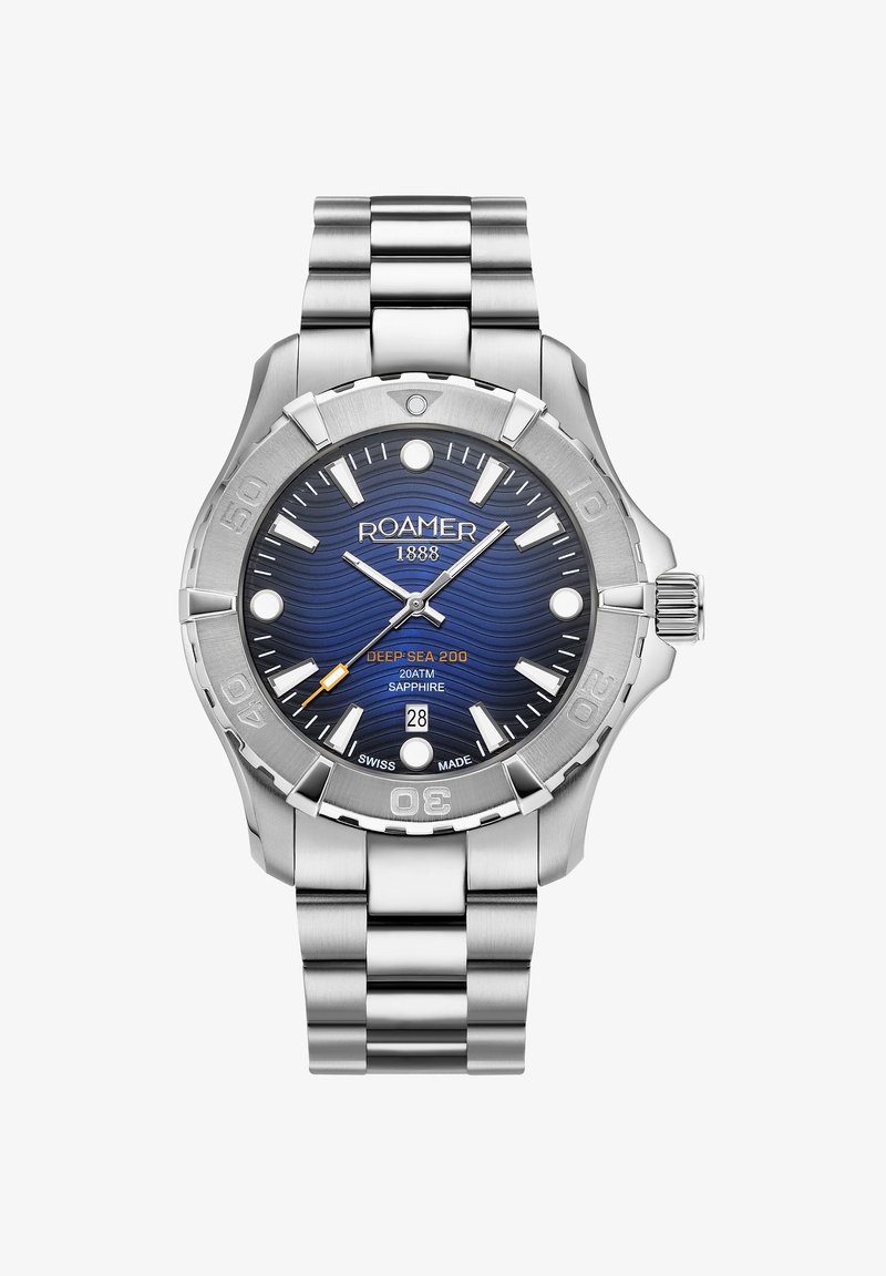 Nerūsējošā tērauda pulkstenis ar zilu viļņu rakstu ciparnīcu, sudraba stundu marķieriem, oranžu akcentu, datuma rādītāju un metāla aproci.