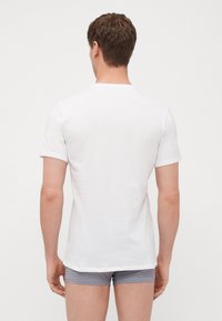 T-shirt blanc à manches courtes affiché de dos, avec un col rond et une texture de tissu doux. Porté avec un short gris à motifs.