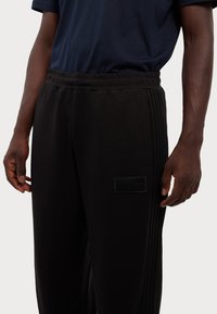 Black jogger pants with a smooth texture, featuring a side logo patch and vertical ribbed accents along the legs. Elastic waistband included.