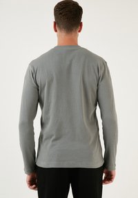 Hosszú ujjú bordázott póló szürke színben, kerek nyakkal és testhez simuló szabással. Texturált anyag, mintázat nélküli egyszerű dizájn.