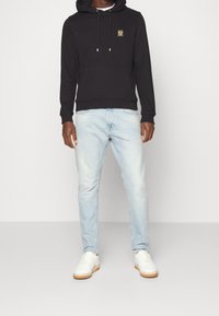 Musta huppari, jossa on logopatchi, yhdistetty vaaleansinisiin farkkuihin. Asusteissa on kengurun tasku ja valkoiset tennarit kumipohjalla.