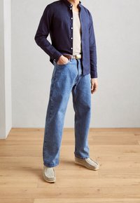 Granatowa koszula z guzikami, szary top na ramionkach, niebieskie dżinsy i jasnoszare mokasyny. Cechy obejmują luźny krój i klasyczne style.