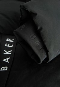 Linge de lit noir présentant un duvet plié avec une texture lisse. Une sangle élastique affiche le mot "BAKER" en lettres blanches.