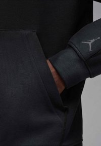 Czarna sportowa bluza z kieszenią typu kangur. Posiada ściągacze na mankietach oraz małe szare logo na rękawie. Gładka, miękka w dotyku tkanina.