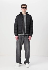Black puffer jacket with quilted design, grey sweater underneath, faded grey jeans, and white sneakers, accessorized with sunglasses.