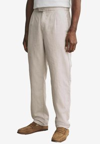 Pantalons en lin beige clair avec une coupe droite, dotés de plis, de poches latérales et d'une finition douce et texturée. Assortis à des mocassins marron.