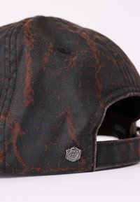 Șapcă neagră cu suprafață texturată ce prezintă un model marmorat maro și un emblemă de trandafir argintiu pe lateral. Curea ajustabilă în partea din spate.