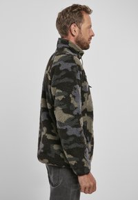 Giacca in pile con motivo mimetico nei colori marrone, verde e grigio; presenta un colletto alto, una tasca sul petto con zip e una texture morbida.