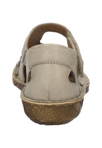 Beige leather sandal with open design, flat comfort sole, and embossed floral pattern on the brown outsole. Adjustable back strap.