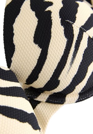 Lähikuva musta-beige raidallisen seepra-kuosisen kankaan tekstuurista, jossa näkyy kaarevat reunat ja ompelun yksityiskohdat.