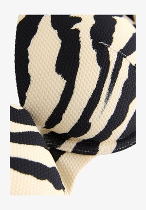 Lähikuva musta-beige raidallisen seepra-kuosisen kankaan tekstuurista, jossa näkyy kaarevat reunat ja ompelun yksityiskohdat.