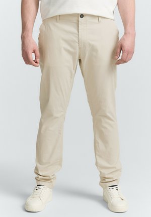 Beige, leichte Chinos mit geradem Bein, Fronttaschen, einem einzelnen Knopfverschluss und dezenten Nähten. Kombiniert mit weißen Sneakers.